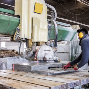 Blue-collar worker cutting granite slab on electric marble saw