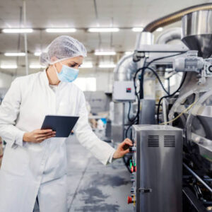 A female milk plant operator holding tablet and adjusting milk processing machine during corona virus.