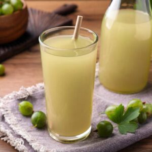 Tasty gooseberry juice in glass on wooden table